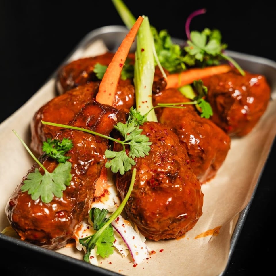 Vegan meatballs in a rich red sauce, garnished with fresh cilantro, carrots, and green onions.