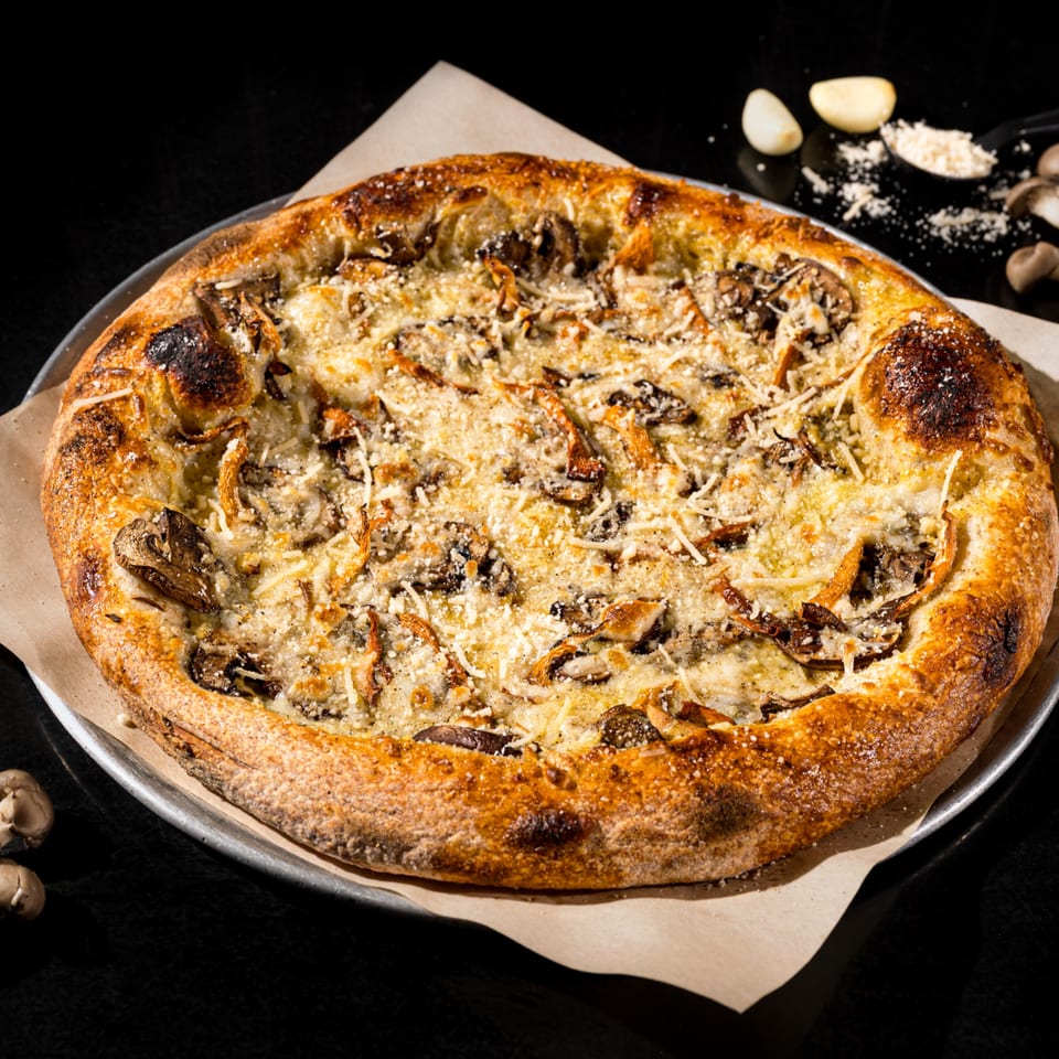 Vegan mushroom pizza with a golden crust, topped with cheese and herbs, on a dark surface.