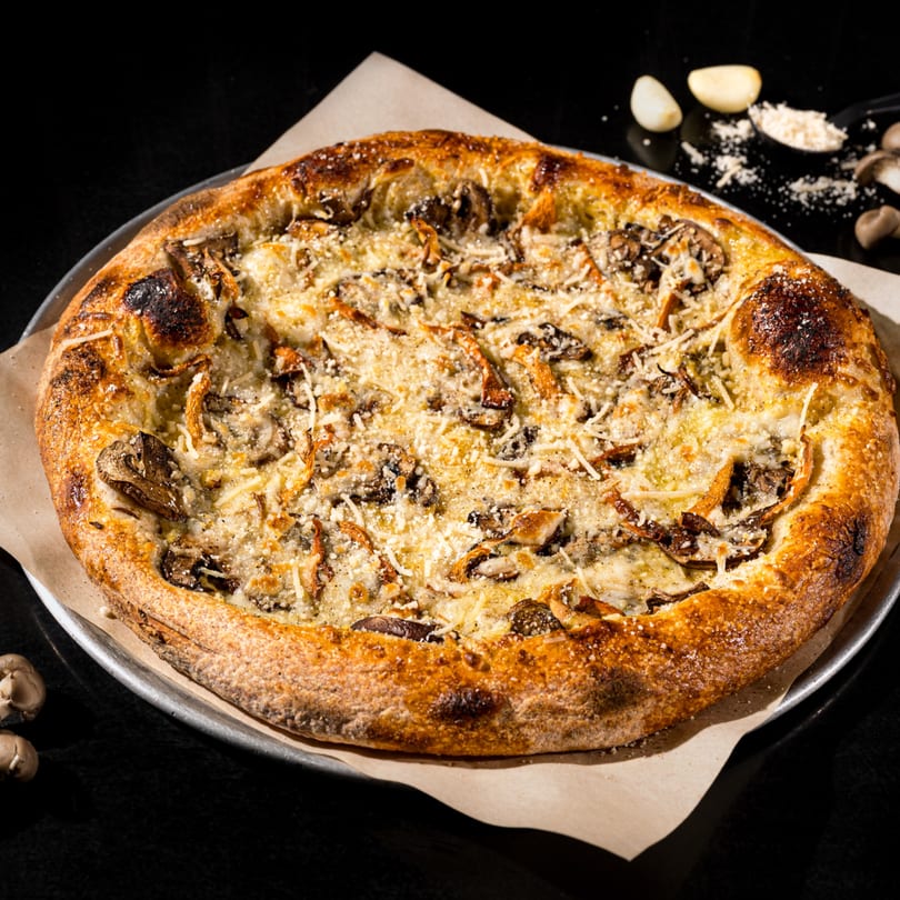 Vegan mushroom pizza with a golden crust, topped with cheese and herbs, on a dark surface.