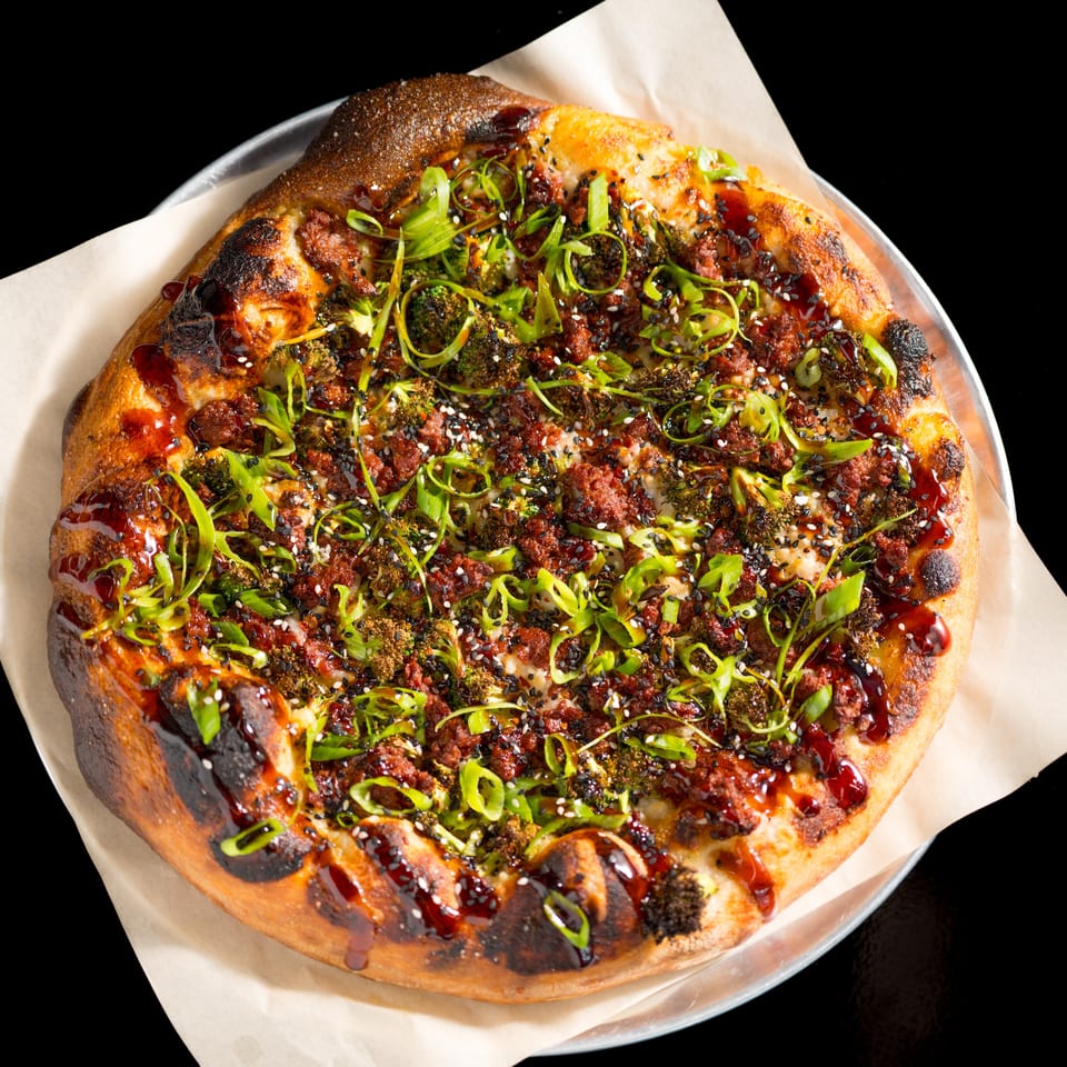 Vegan pizza from Down 2 Earth Pizzeria, topped with plant-based meat, broccoli, scallions, and sesame seeds.